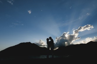 Silhouettes of a man and a woman who hug and kiss at sunset on the seashore against the background