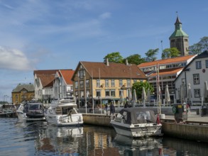 A harbour with several boats in front of colourful buildings under a blue sky with few clouds,