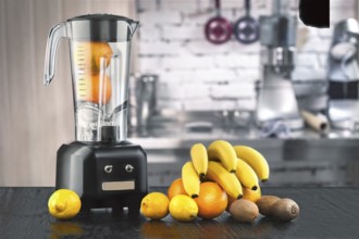 Metal food blender close-up with fresh exotic tropic fruits next to it on kitchen background with