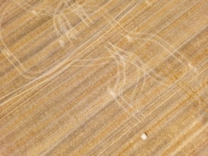 Striking tracks and patterns from a tractor on a dry agricultural field with straw bales, aerial