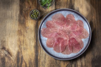 Food, Marbled beef for carpaccio with ingredients arugula and capers on gray plate, wooden
