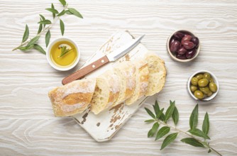 Sliced fresh ciabatta on cutting kitchen board, green and brown olives, olive oil with rosemary,