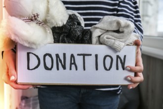 Female volunteer holding donation box with old used toys and clothes indoors. Happy Charity.