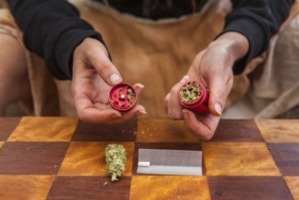 Selective focus closeup of person's hands holding a red weed filled grinder shot from above.