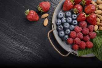 Tray with ripe organic bilberry raspberry strawberry and almonds set on slate closeup