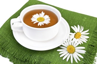 Herbal tea in a white cup with daisies on the green napkin, isolated on a white background