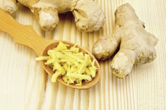 Wooden spoon with grated ginger, ginger root against a wooden board