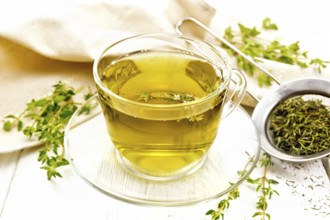 Herbal tea in a glass cup of thyme, a metal strainer with dry leaves, a linen napkin on the