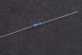 A blue-striped resistor with long leads on a dark background