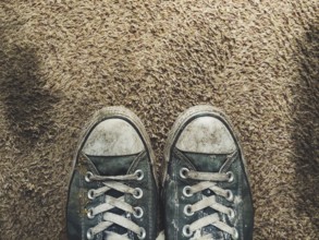 Pair of worn out black sneakers on brown carpet