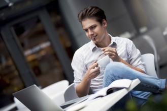 Handsome caucasian young man working on laptop and smiling while enjoying coffee in cafe