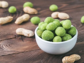 Peanut snack for beer, wine, party bar. Salted peanuts in green vasabi glaze on brown wooden table.