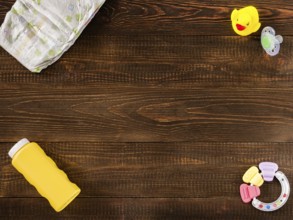 Disposable diaper, teether, dummy, baby powder and rubber duckling on dark wooden background with