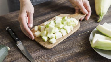 Zucchini harvest. Woman slices zucchini cubes for freezing on wooden table. Farm organic zucchini