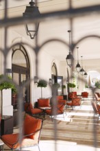 View through the wrought-iron lattice onto the hotel terrace with soft chairs and tables.