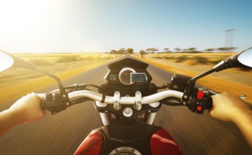 Biker driving a motorcycle rides along the country road, morning scene . First person angle view