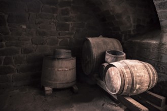 Vintage image with the interior of a stone wine cellar and aged wooden barrels, in low light.