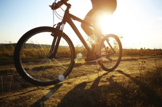 Male cyclist driving by rural dirt road outdoors. Low angle view