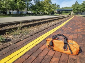 Waiting for a train concept - a bright orange duffel on a station platform behind yellow line