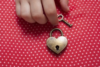 Hand holding a heart shaped lock and key on a red background