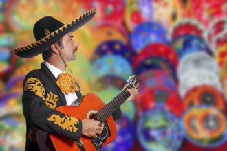 Charro Mariachi playing guitar over colorful blur handcrafts background