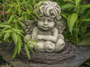 Angel statue in a nest of twigs, surrounded by green leaves in the garden, borken, münsterland,