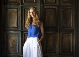 Portrait of the blonde woman in blue blouse staying in front of dark wall and keep smiling