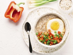 Savory oatmeal in craft trendy bowl, served with vegetables and fried egg on white concrete