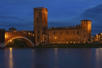 Majestic castle with bridge illuminated against the night sky with mirror-smooth river, at the blue