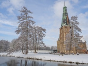Castle with high tower in winter. Snow-covered trees and a frozen lake in the foreground, Raesfeld,