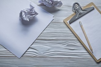 Crumpled paper balls and small clipboard with pencil on vintage white wooden boards