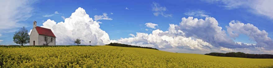 Panorama, chapel and storm clouds over a rapeseed field