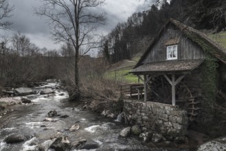 Vintage landscape with an old, abandoned water mill on an alpine river shore, on a cloudy day of