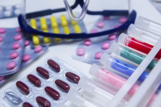 An arrangement of colorful pills and test tubes with safety glasses nearby