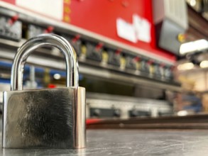 Image of a metal padlock in the foreground against the background of a metal bending machine.