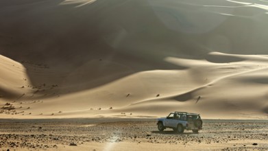 An off-road vehicle drives through softly lit dunes in a vast desert landscape, Off-road vehicle