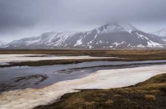 Icelandic landscape with frozen lake, mountains and meadow land covered in snow at snaefellsnes