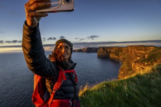 Female hiker taking a selfie, Cliffs of Moher, The Burren, County Clare, Ireland, United Kingdom,