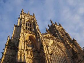 A front view of the towers at the entrance to york minster in sunlight against a blue cloudy sky