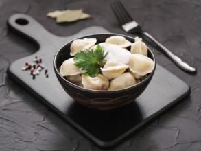 Traditional russian pelmeni, ravioli, dumplings with meat on black cutting board over black