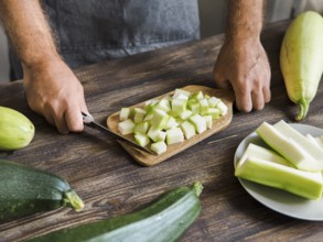 Zucchini harvest. Man slices zucchini cubes for freezing on wooden table. Farm organic zucchini
