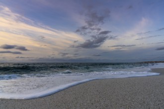 A low angle view of white sand beach with waves rolling in under a colorful sunset sky