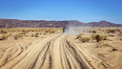 An off-road vehicle drives on a dusty sandy track in an arid desert, With the off-road vehicle