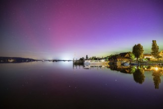 In a calm lake, the vivid northern lights are reflected next to boats and trees, harbour,