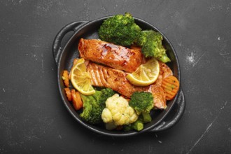 Healthy baked fish salmon steaks, broccoli, cauliflower, carrot in cast iron casserole bowl black