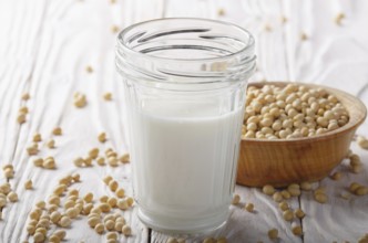 Non-dairy alternative Soy milk or yogurt in mason jar on white wooden table with soybeans in bowl