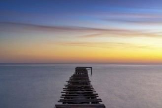 Peaceful sunrise seascape with an old wooden dock leading out into the calm ocean waters