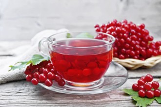 Tea with viburnum in a glass cup, wicker plate with berries, green leaves and a burlap napkin on