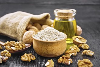 Walnut flour in bowl, nuts on a table, in a spoon and in a bag, oil in glass jar on wooden board