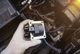 Hand holds car part with engine components around, highlighted by warm lighting